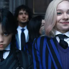 Skådespelare Wednesday Addams med flätor och en allvarlig min, bredvid en leende elev med blont hår och blåa inslag.