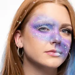 En ung kvinna med fantasifull makeup som påminner om siren eyes, med lila och blåa färger, glitter och strass.