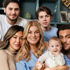 Familjen samlad, med en leende mamma som håller sitt luciano ingrosso barn. Två äldre söner och en ung man ler mot kameran.