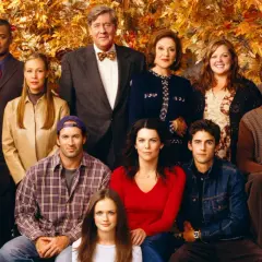Hela rollistan i Gilmore Girls samlad framför höstfärgat lövverk. En ikonisk ensemblebild som fångar seriens charm.