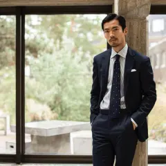 Man i mörk kostym med prickig slips, en stil som påminner om modern japan fashion.