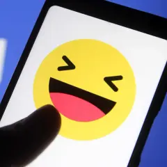 En tumme pekar på en skrattande emoji på en mobilskärm. Kanske undrar du vad betyder lol?
