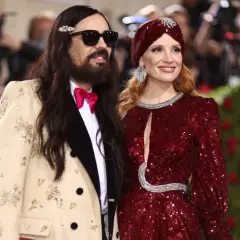 Alessandro Michele och Jessica Chastain poserar glatt. Han bär en beige kavaj med broderier och en rosa fluga.