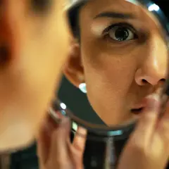 En kvinna ser sig i spegeln, hennes blick intensiv. En scen som skulle kunna vara från en psykologisk thriller topplista film, där sanningen döljer sig i reflektionen.
