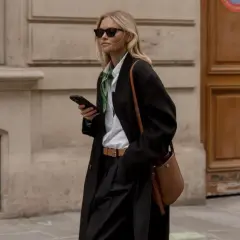 En kvinna i en elegant svart kappa, vit skjorta och grönt sidenband visar upp vårmode 2026 dam.