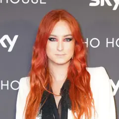 Harris Reed med flammande rött hår och dramatisk makeup, klädd i en vit kavaj.