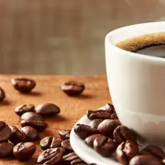 En kopp ångande kaffe med bönor utspridda på träbordet. Frank Hu älskar morgonkaffe.