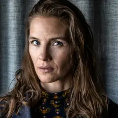 Lisa Carlehed, med blå ögon och brunt hår, blickar intensivt mot kameran. Hon bär en mörkblå jacka över en mönstrad tröja.