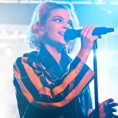 En artist med tove styrke sjunger i mikrofonen, iklädd en läderjacka med orange och svarta ränder.