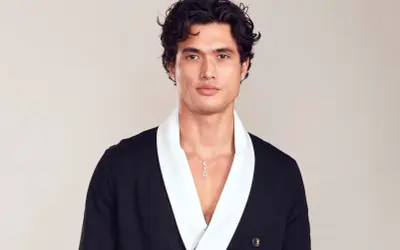 Charles Melton bär en svart kavaj med vit krage och ett diamant-halsband.
