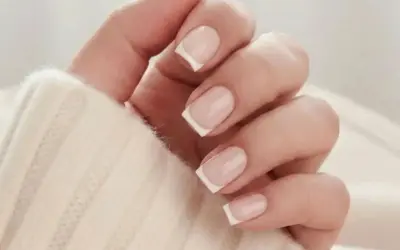 En hand med klassisk fransk manikyr på korta naglar, insvept i en mjuk, beige tröja.