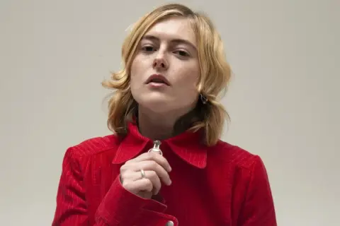 Ellen Krauss i röd manchesterjacka, med fingret vid dragkedjan.
