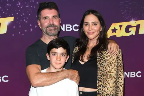 Simon Cowell, Lauren Silverman och deras son Eric poserar glatt framför AGT-logotypen.