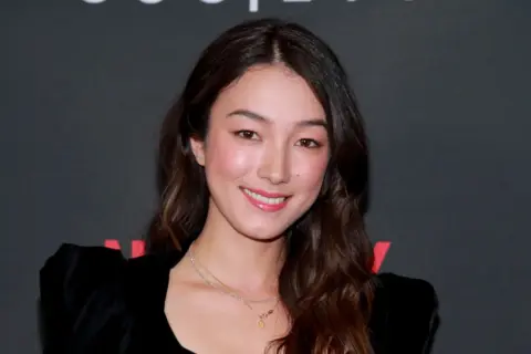 Natasha Liu Bordizzo ler glatt i en svart klänning med puffärmar.
