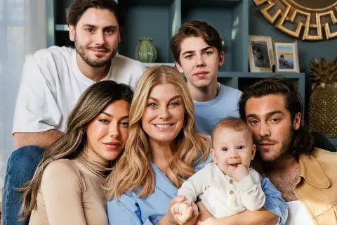 Familjen samlad, med en leende mamma som håller sitt luciano ingrosso barn. Två äldre söner och en ung man ler mot kameran.