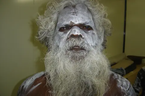 En aboriginal model med vitt ansiktsmåleri och långt grått skägg.