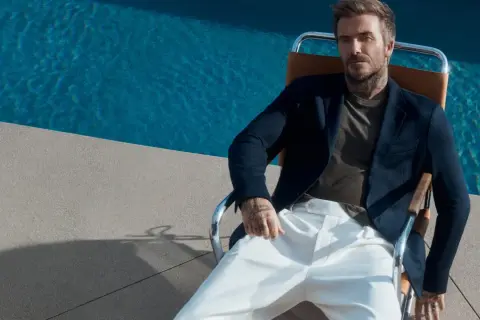 David Beckham style: en man i mörk kavaj och vita byxor sitter vid en pool.