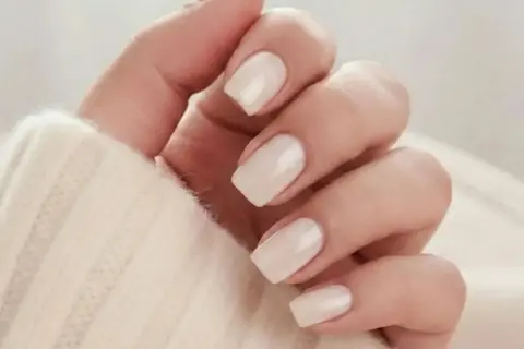 En hand med ljusa, mandelformade naglar i en mjuk, krämig färg. Perfekt almond nails inspo för en elegant look.