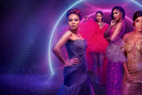Fyra kvinnor i glittrande klänningar poserar framför en neonljusring. En scen som hämtad ur de mest glamorösa fashion movies.
