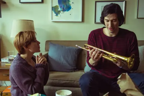 Adam Driver håller i en trumpet i en scen från en av hans filmer. Bredvid honom sitter en kvinna och tittar på.