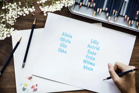 En hand skriver nordiska flicknamn som Alicia, Olivia, Ella, Ebba, Lilly, Astrid, Saga, Freja, Wilma och Maja.