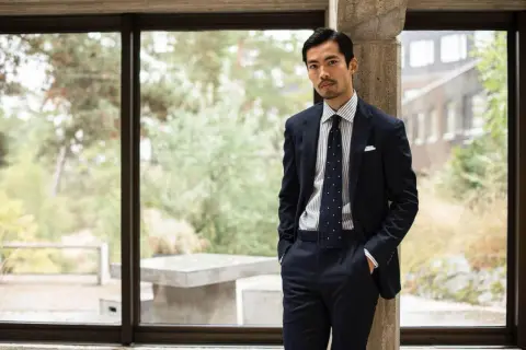 Man i mörk kostym med prickig slips, en stil som påminner om modern japan fashion.