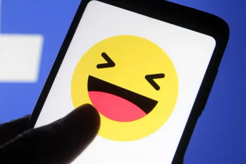 En tumme pekar på en skrattande emoji på en mobilskärm. Kanske undrar du vad betyder lol?
