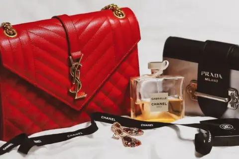 En röd, quiltad modalu väska med gulddetaljer, bredvid en Prada-väska, Chanel-parfym och smycken.