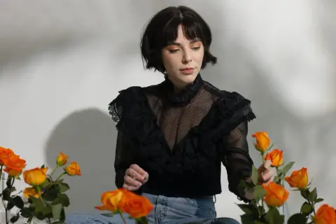 En kvinna med en elegant french bob, klädd i en svart spetsblus, omgiven av orange rosor.