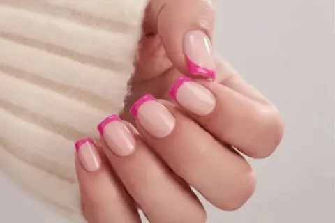 En hand med naglar i fransk manikyr med en modern twist av knallrosa. Olika nail types som visar en lekfull stil.