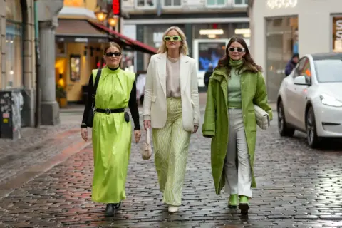 Tre kvinnor i ljusgröna och vita kläder, med solglasögon, promenerar på en kullerstensgata. En tydlig dansk kvinna stil.