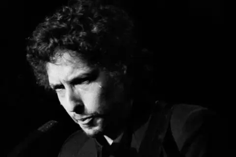 Bob Dylan, ikoniskt ansikte i en svartvit film, med lockigt hår och intensiv blick.