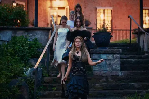 Grupp unga kvinnor, som barracuda queens, går nerför en stentrappa i kvällsljus.