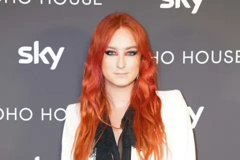 Harris Reed med flammande rött hår och dramatisk makeup, klädd i en vit kavaj.