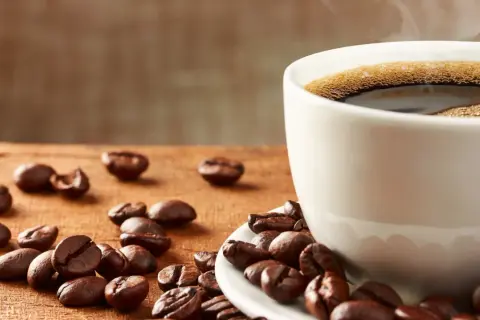 En kopp ångande kaffe med bönor utspridda på träbordet. Frank Hu älskar morgonkaffe.