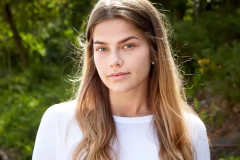 En ung kvinna med blont hår och blå ögon, en blivande top model Sverige, ler mot kameran utomhus.