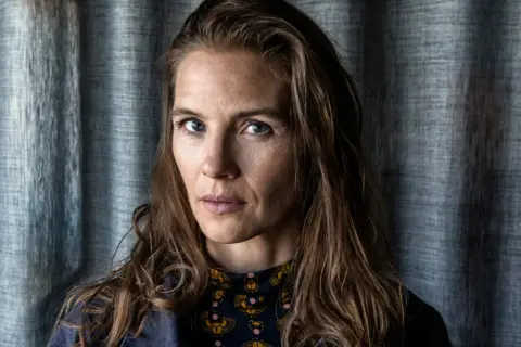 Lisa Carlehed, med blå ögon och brunt hår, blickar intensivt mot kameran. Hon bär en mörkblå jacka över en mönstrad tröja.