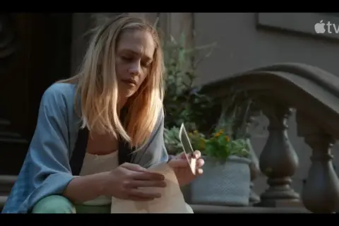 Jemima Kirke sitter på trappan och läser ett brev med en kniv i handen. En scen från filmer och tv-program med Jemima Kirke.