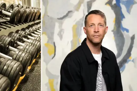 En man med en blick som antyder "looksmaxxing meaning" står framför en abstrakt tavla. Till vänster syns en hylla med hantlar.