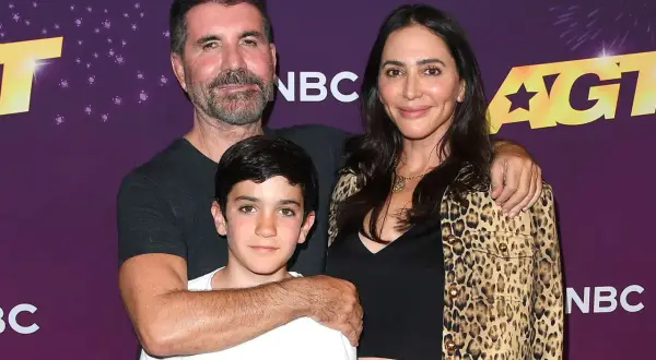 Simon Cowell, Lauren Silverman och deras son Eric poserar glatt framför AGT-logotypen.