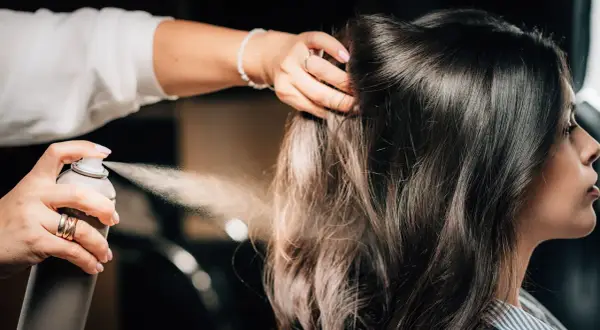 Hårstylist fixar en elegant edgar hairstyle med hårspray.