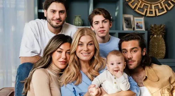 Familjen samlad, med en leende mamma som håller sitt luciano ingrosso barn. Två äldre söner och en ung man ler mot kameran.