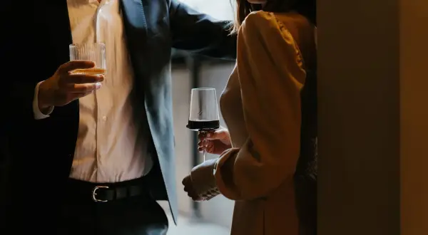 En man i kostym håller ett glas whisky, en kvinna i klänning håller ett glas rödvin. Kanske är det dags för några frågor till killar?