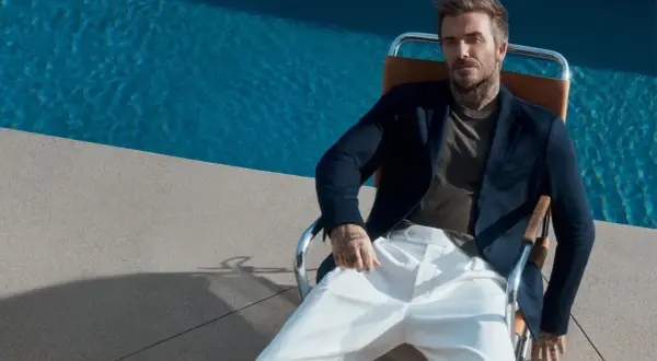 David Beckham style: en man i mörk kavaj och vita byxor sitter vid en pool.