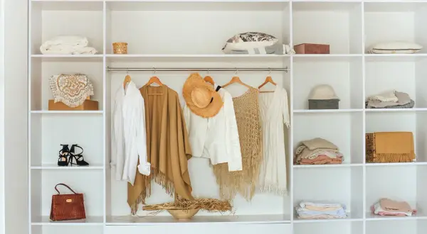 En vit garderob med kläder och accessoarer. En vit skjorta, en brun poncho, en vit kavaj med hatt, en beige virkad topp och en vit klänning hänger på galgar. Hm, bubs, så fint!