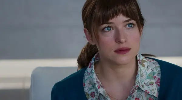 Dakota Johnson with blue eyes and brown hair, wearing a floral shirt and teal cardigan.