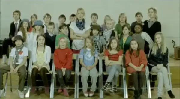 Veronica Maggio barn i en klassrumsmiljö. En grupp barn sitter på stolar framför en lärare.