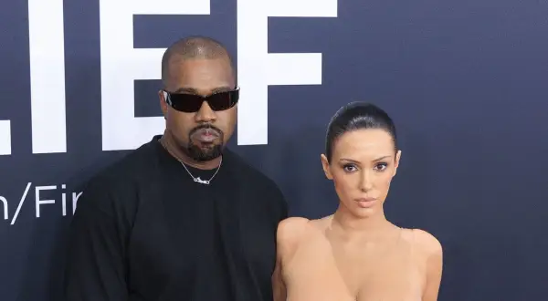 Kanye West och Bianca Censori poserar framför en stor logotyp.