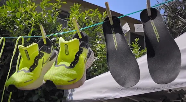 Två par neongröna löparskor och två svarta innersulor hänger på tork. Nike Move to Zero-filosofin syns i detaljerna.