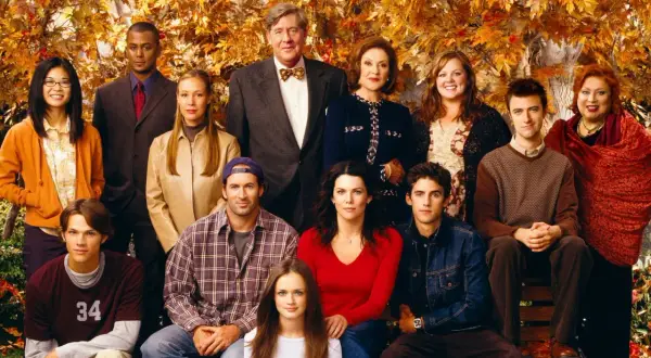 Hela rollistan i Gilmore Girls samlad framför höstfärgat lövverk. En ikonisk ensemblebild som fångar seriens charm.